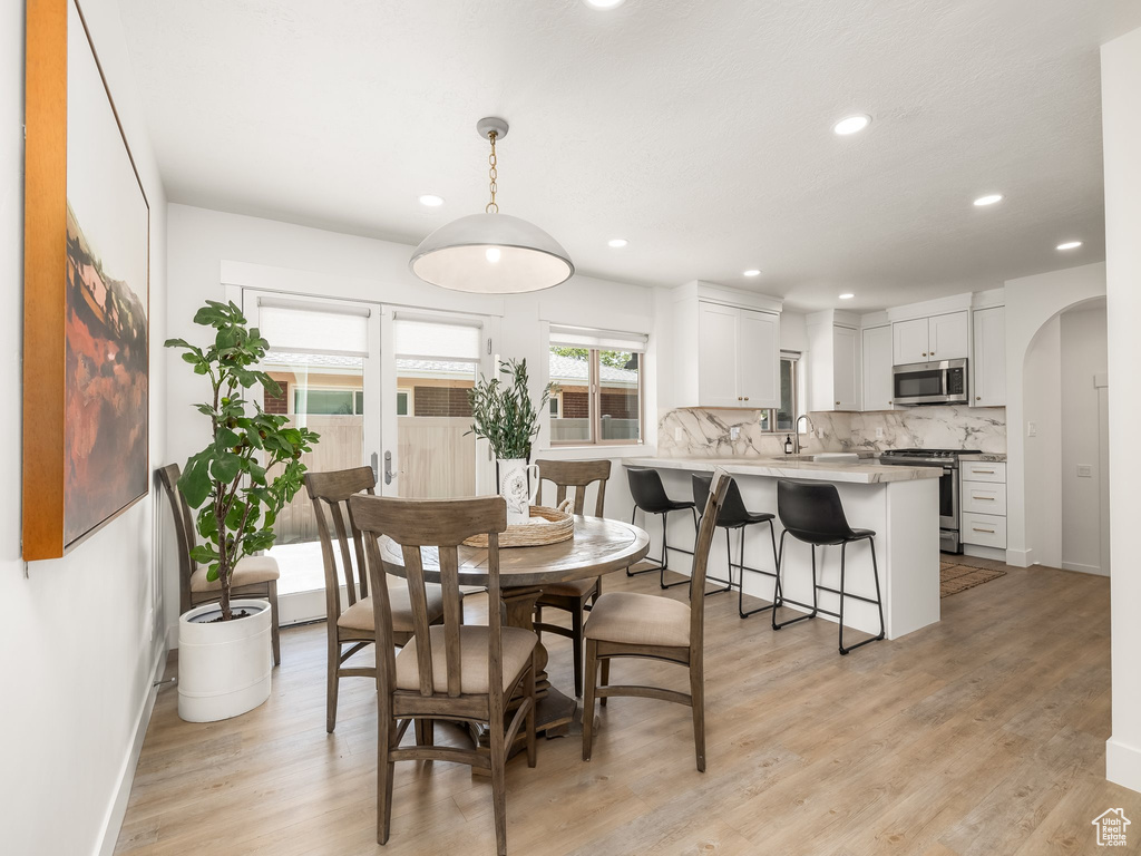 Dining space featuring arched walkways, light wood finished floors, baseboards, and recessed lighting