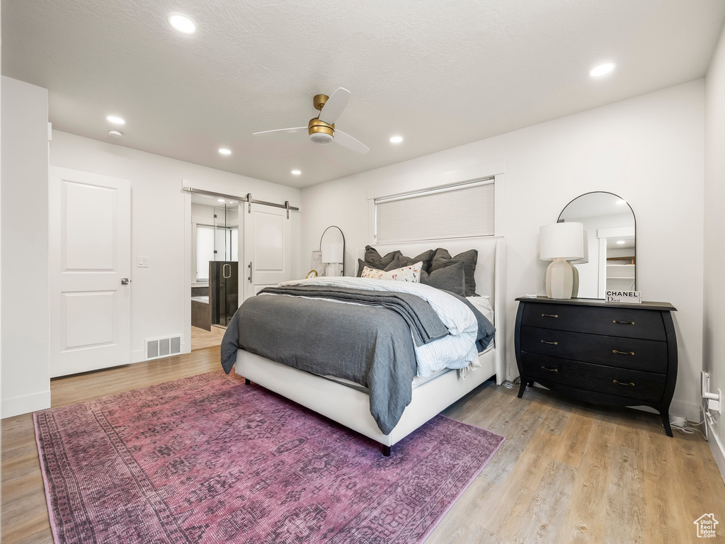 Bedroom with a barn door, light wood-type flooring, recessed lighting, a ceiling fan, and baseboards
