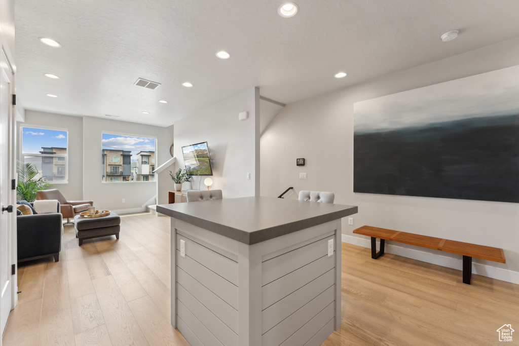 Kitchen featuring light wood finished floors, dark countertops, a kitchen island, recessed lighting, and baseboards