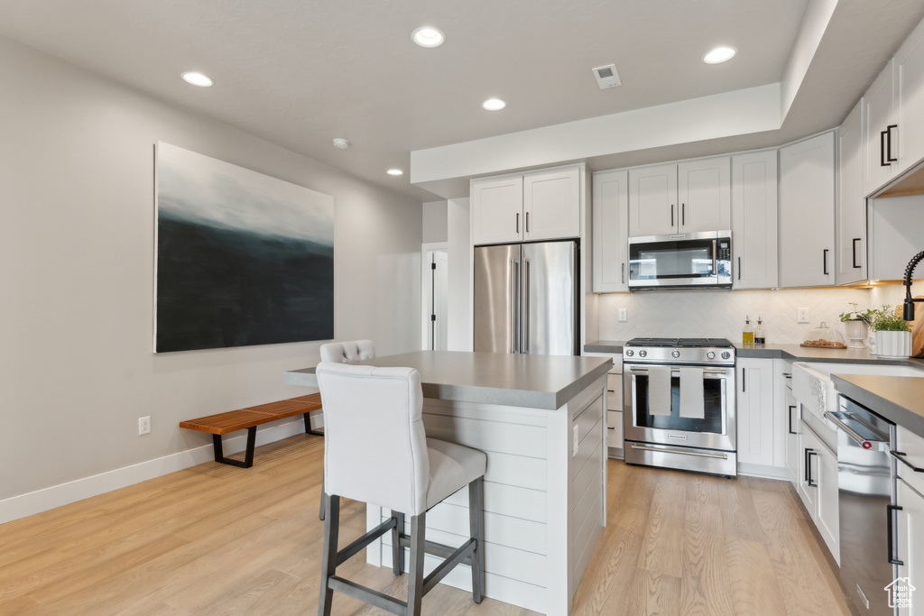 Kitchen with stainless steel appliances, light wood-style flooring, a kitchen bar, a sink, and recessed lighting