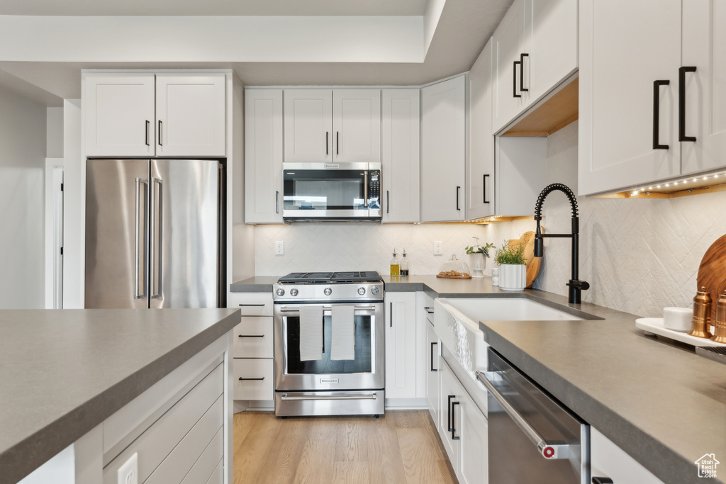 Kitchen featuring stainless steel appliances, a sink, dark countertops, white cabinets, and decorative backsplash