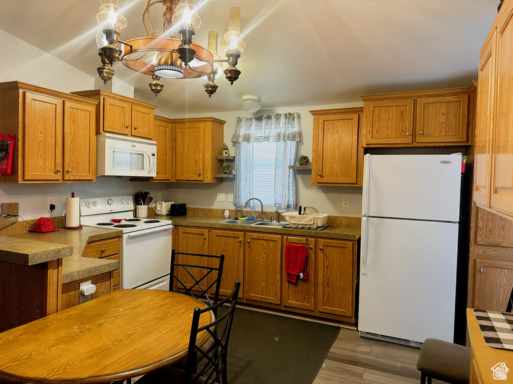 Kitchen with white appliances, a sink, brown cabinets, wood finished floors, and vaulted ceiling