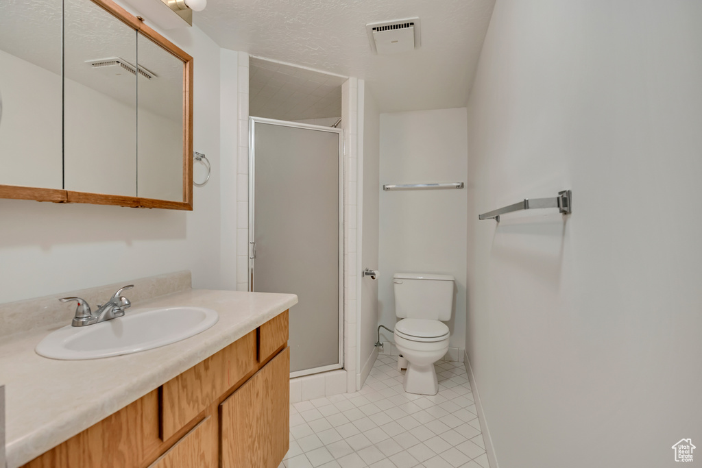 Bathroom featuring toilet, a stall shower, tile patterned floors, and vanity