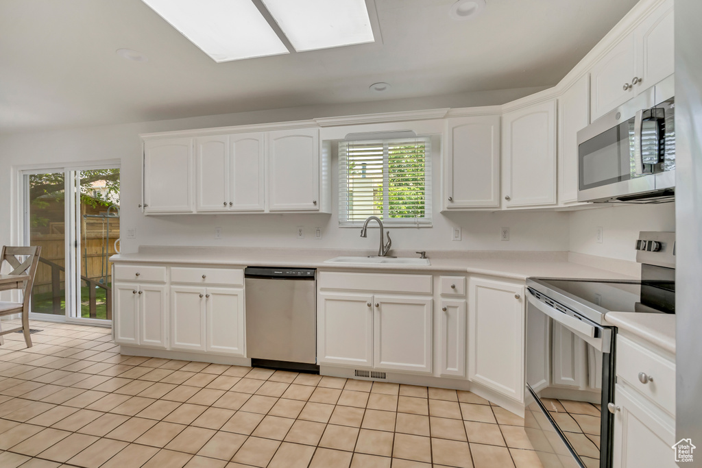 Kitchen featuring stainless steel appliances, a sink, a skylight, white cabinetry, and light tile patterned flooring
