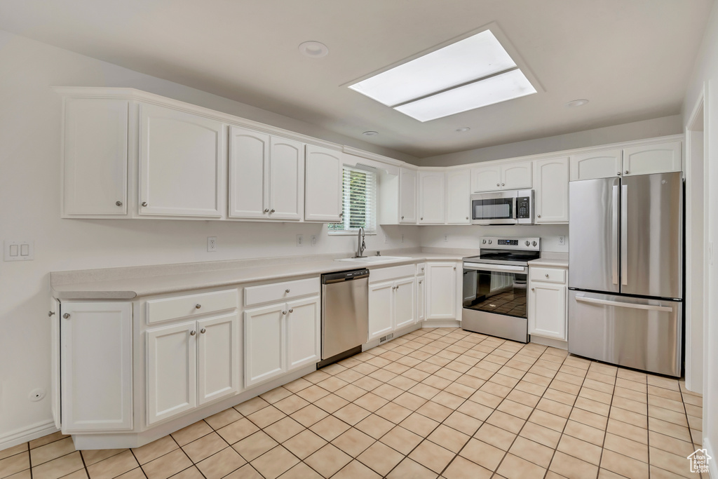 Kitchen featuring appliances with stainless steel finishes, a sink, a skylight, white cabinetry, and light countertops