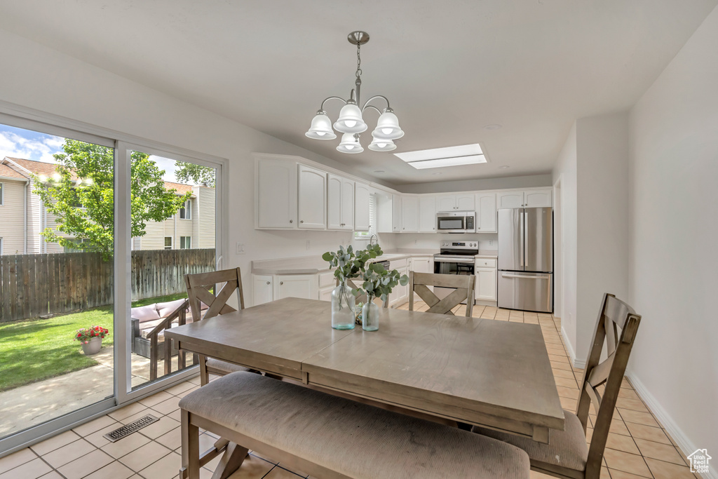 Dining room featuring light tile patterned floors, a chandelier, a skylight, and baseboards