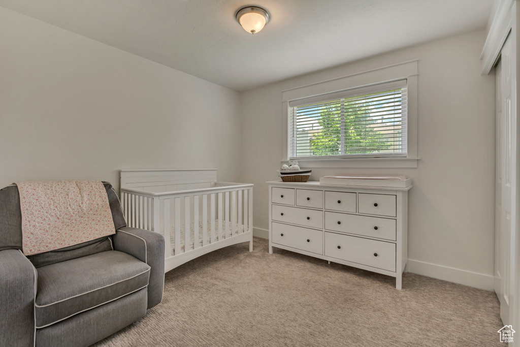 Bedroom featuring light colored carpet, baseboards, and a nursery area