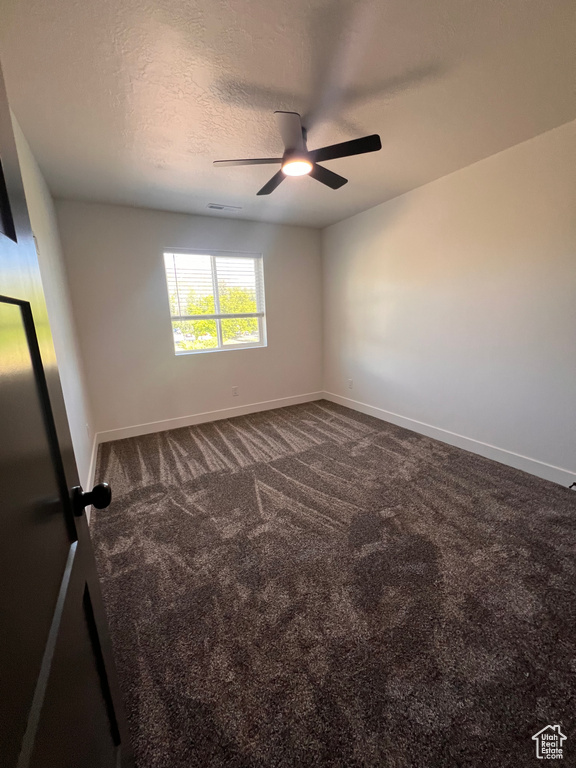 Spare room featuring dark colored carpet, ceiling fan, baseboards, and a textured ceiling