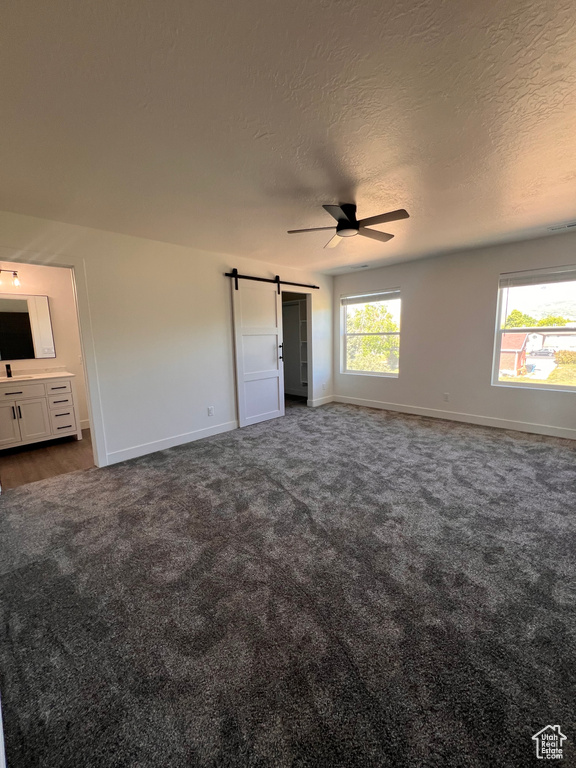 Unfurnished bedroom with a barn door, multiple windows, a textured ceiling, baseboards, and dark colored carpet