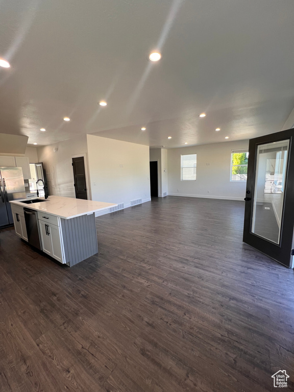 Kitchen with appliances with stainless steel finishes, white cabinetry, open floor plan, a kitchen island with sink, and dark wood-type flooring