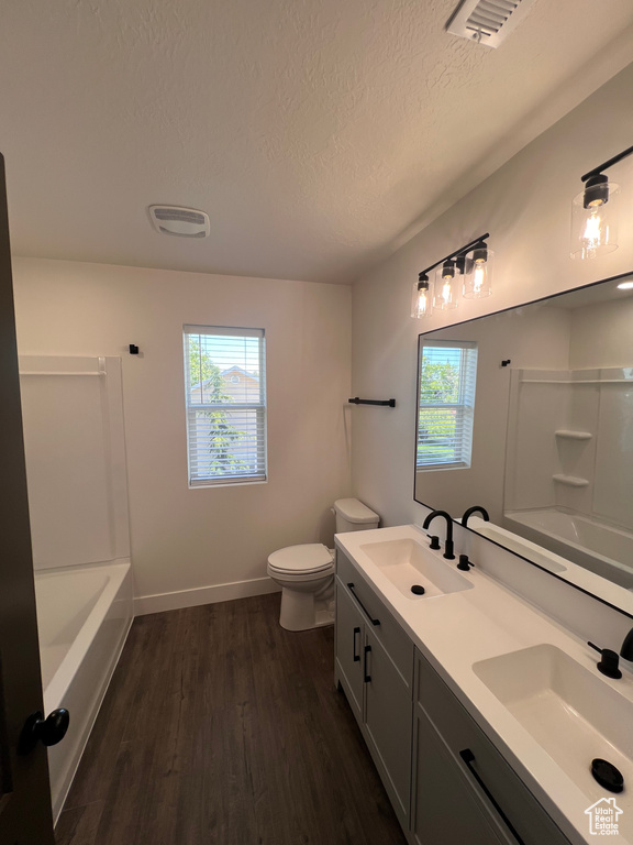 Bathroom with wood finished floors, a textured ceiling, toilet, double vanity, and baseboards