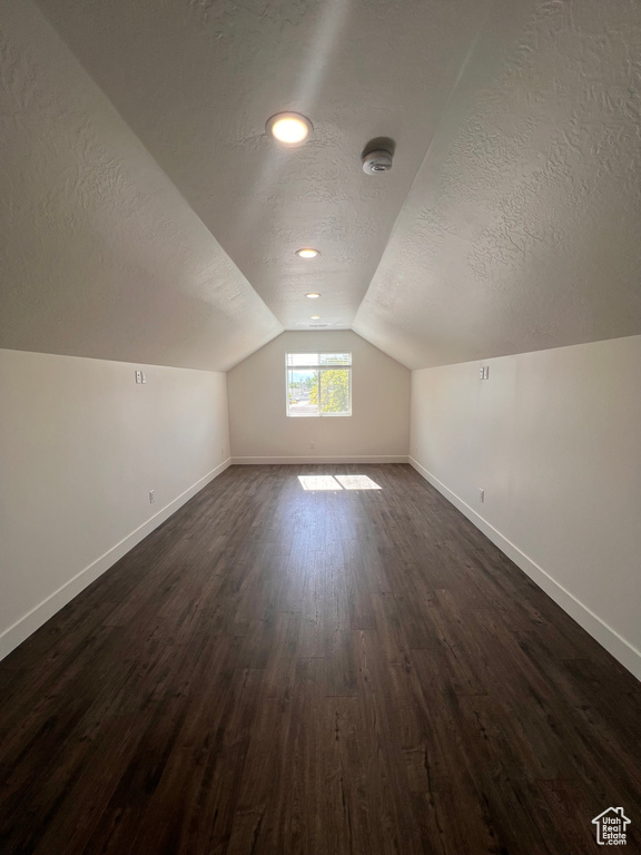 Additional living space with a textured ceiling, baseboards, vaulted ceiling, and dark wood-style flooring