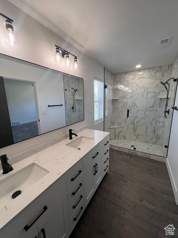 Full bath with a marble finish shower, wood finished floors, and double vanity