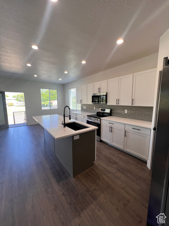 Kitchen featuring appliances with stainless steel finishes, a sink, tasteful backsplash, dark wood-style flooring, and white cabinets