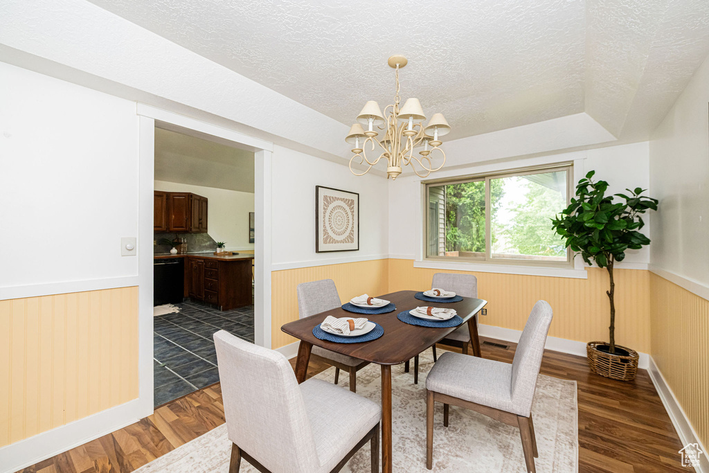 Dining space featuring wainscoting, dark wood-type flooring, a textured ceiling, a chandelier, and baseboards