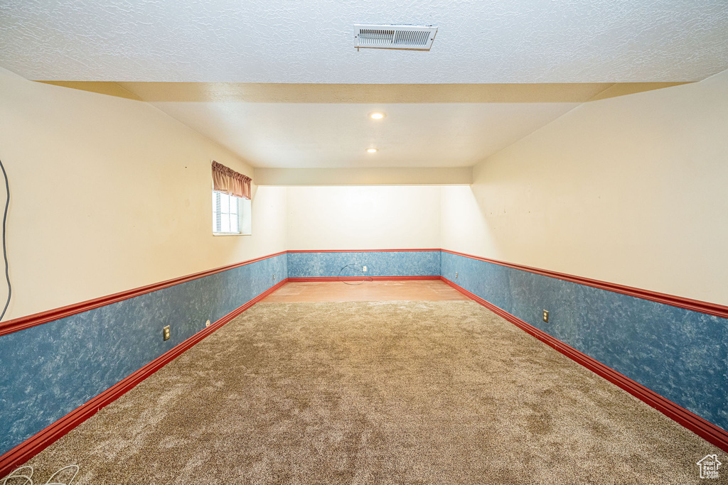 Carpeted empty room featuring a textured ceiling, wallpapered walls, and a wainscoted wall