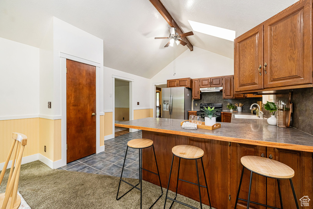 Kitchen featuring stainless steel refrigerator with ice dispenser, range, a sink, a ceiling fan, and under cabinet range hood