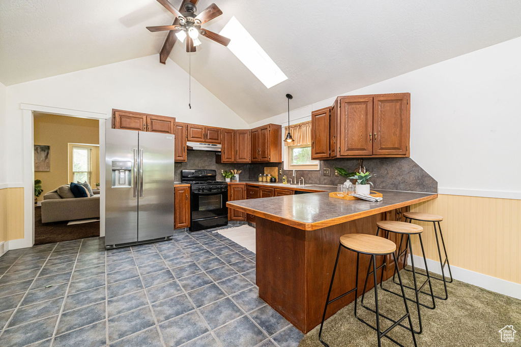 Kitchen featuring stainless steel fridge, black gas range, a skylight, a ceiling fan, and a peninsula
