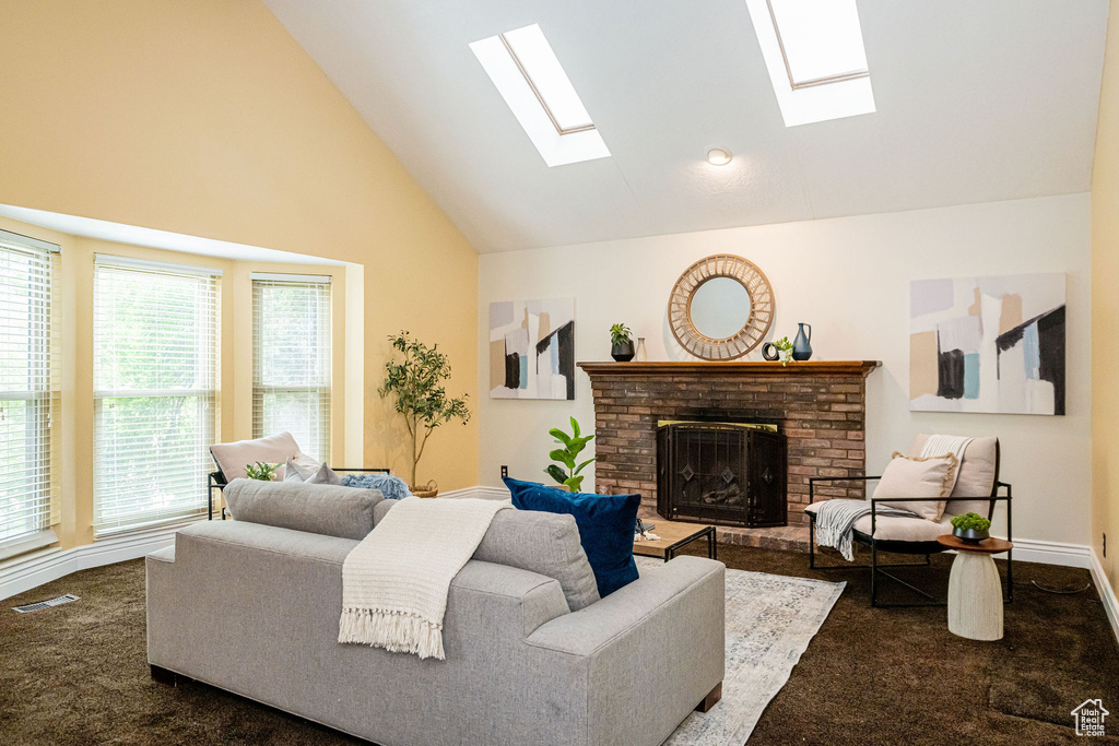 Living room featuring a skylight, dark carpet, high vaulted ceiling, a brick fireplace, and plenty of natural light