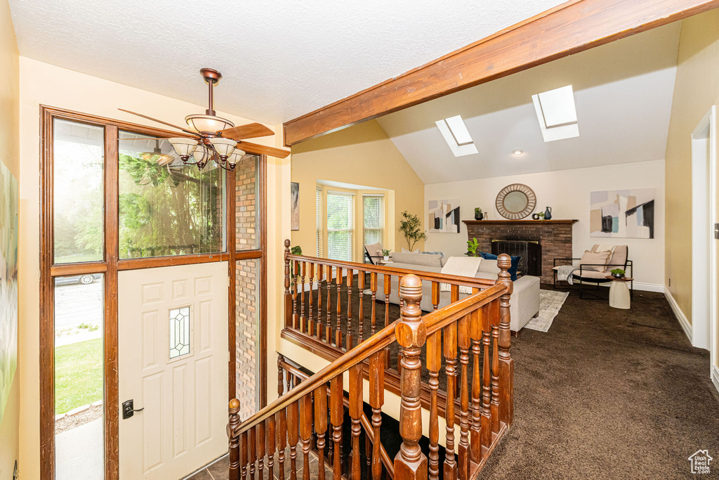 Foyer entrance featuring a fireplace, a skylight, lofted ceiling, dark carpet, and ceiling fan