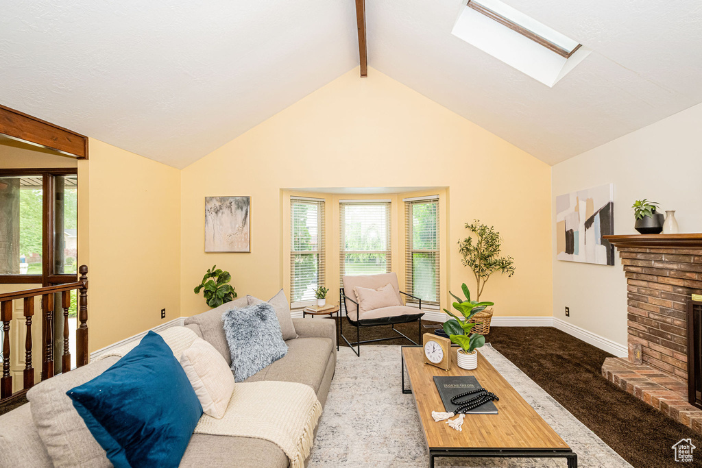 Living area featuring a skylight, beamed ceiling, high vaulted ceiling, a brick fireplace, and carpet flooring