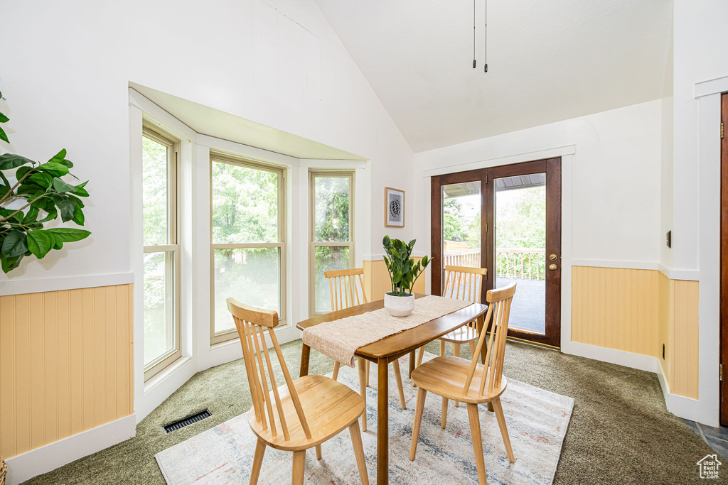 Dining room with plenty of natural light, wainscoting, carpet floors, and high vaulted ceiling