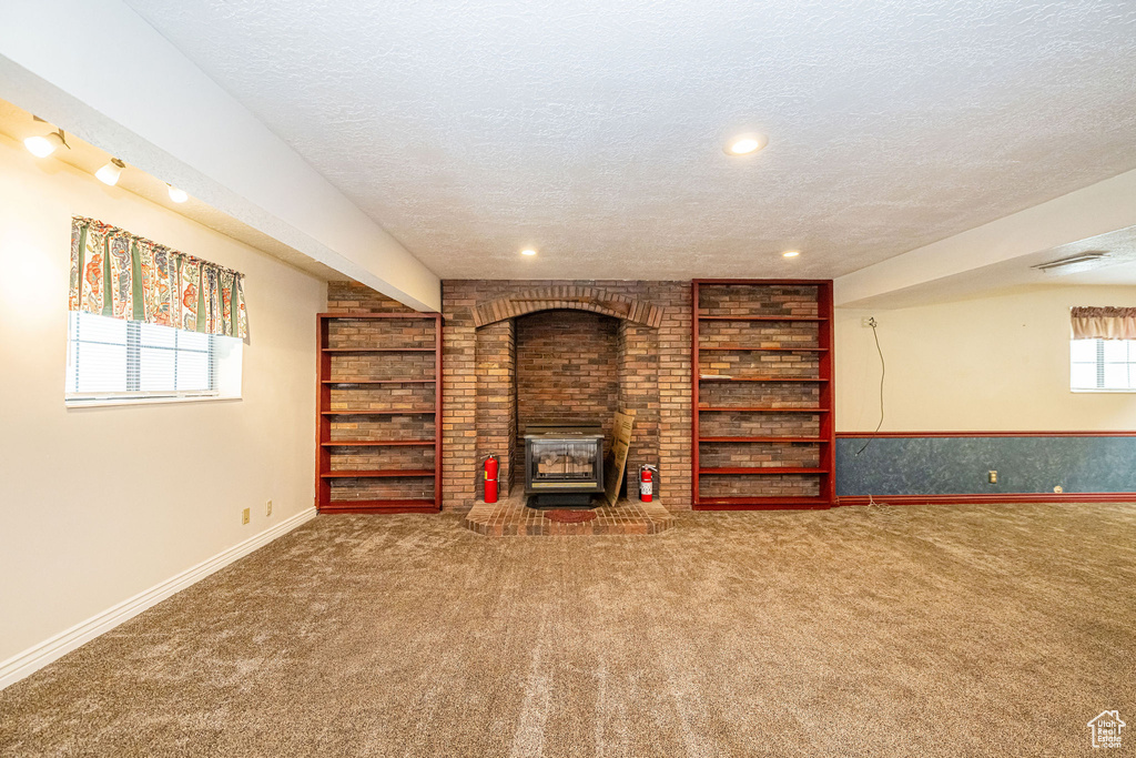 Unfurnished living room featuring a wood stove, a textured ceiling, carpet, built in shelves, and recessed lighting