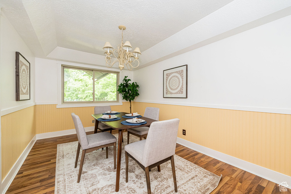 Dining space featuring wainscoting, wood finished floors, a chandelier, baseboards, and a textured ceiling