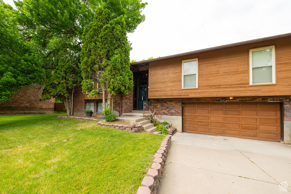 View of front facade with a garage, driveway, a front yard, and brick siding