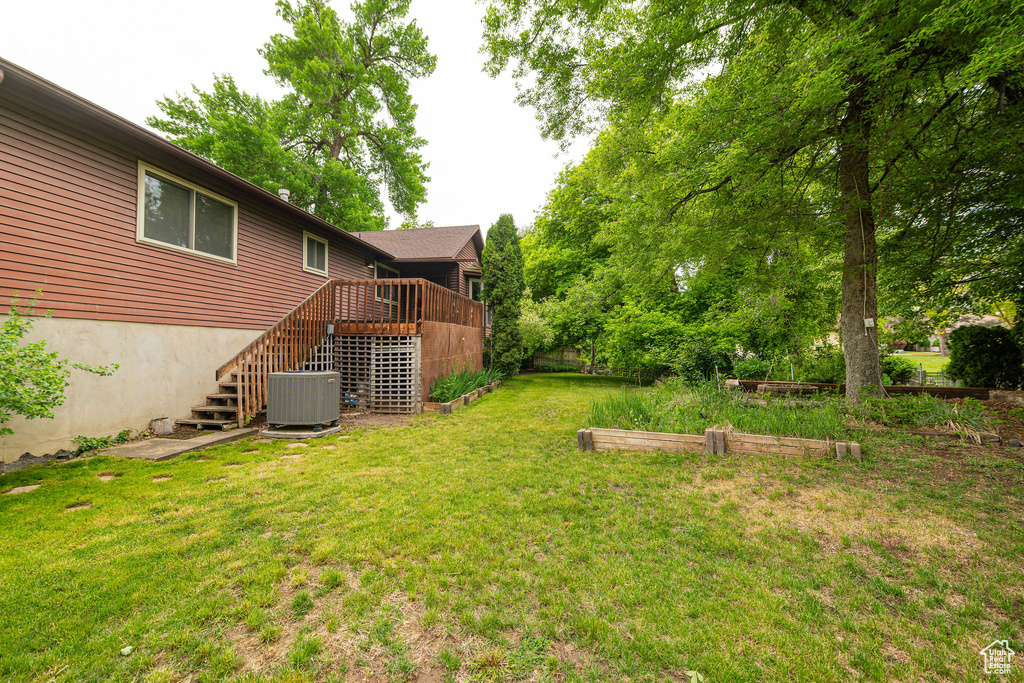 View of grassy yard with stairway, central air condition unit, and a wooden deck
