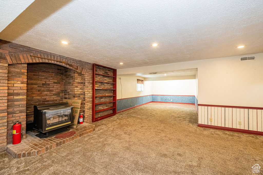 Unfurnished living room with a textured ceiling, carpet floors, a wood stove, recessed lighting, and a wainscoted wall