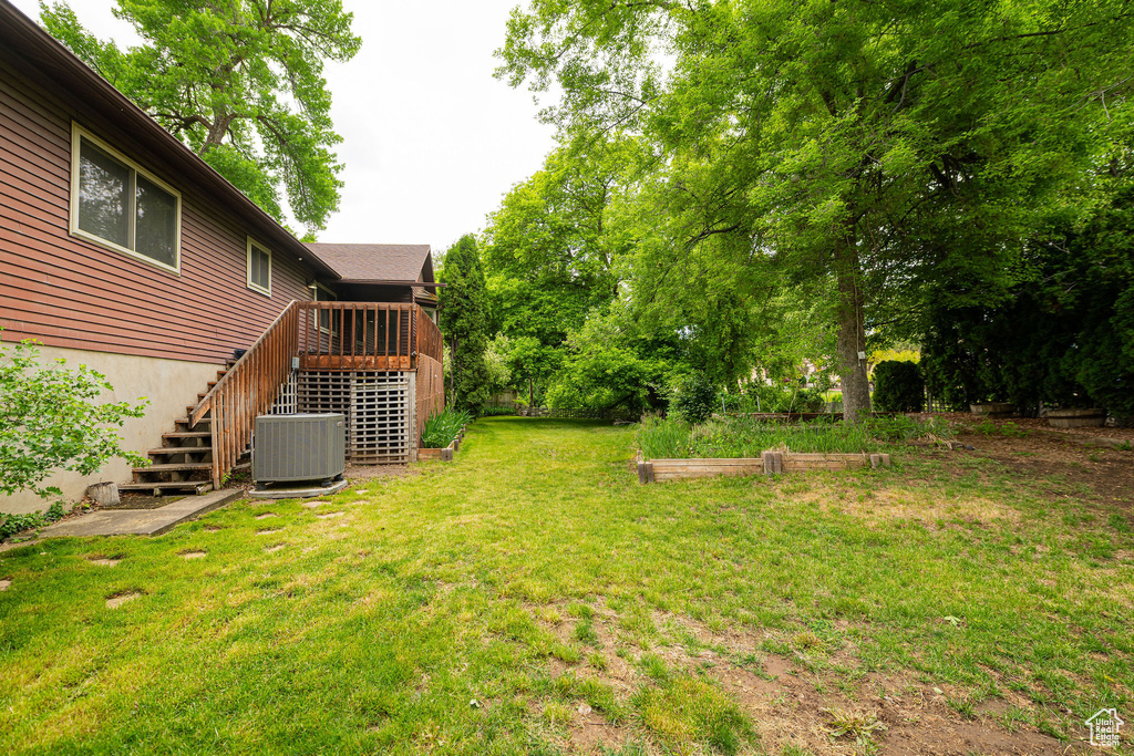 View of grassy yard with stairway, central AC unit, a wooden deck, and a vegetable garden