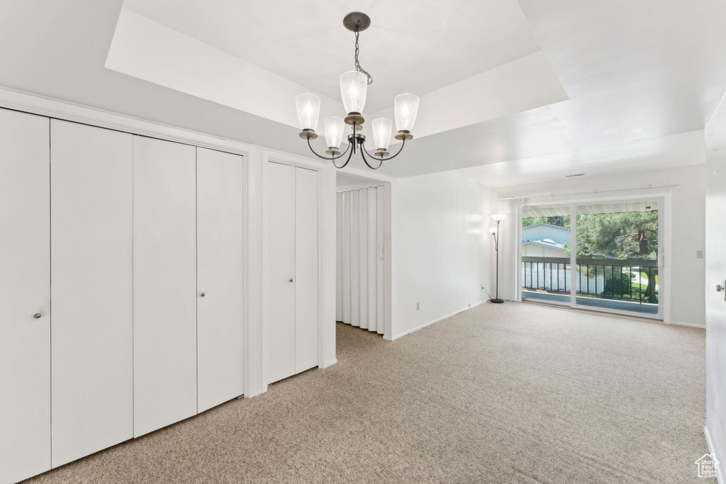 Unfurnished dining area featuring a chandelier, light colored carpet, a raised ceiling, and baseboards