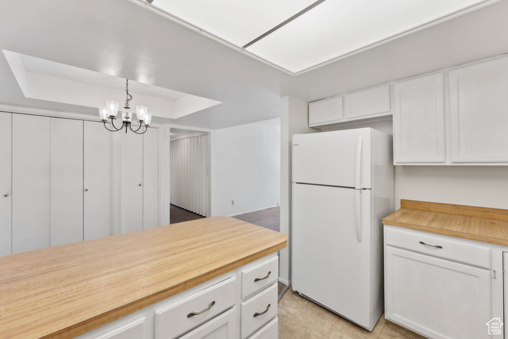 Kitchen featuring freestanding refrigerator, white cabinets, a chandelier, and wooden counters