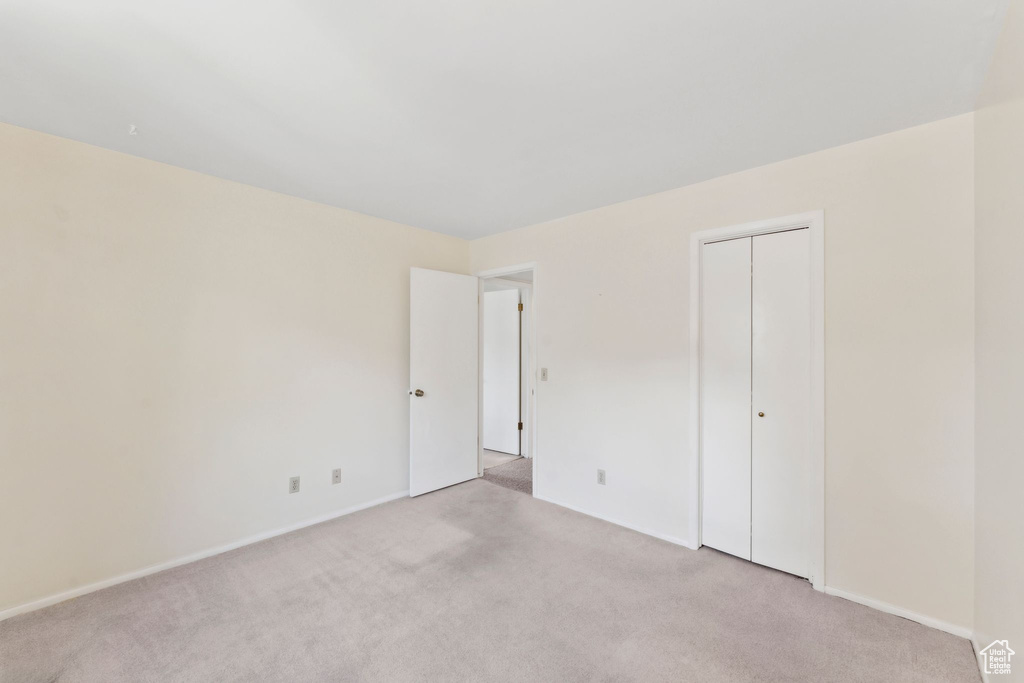 Unfurnished bedroom featuring light carpet, a closet, and baseboards