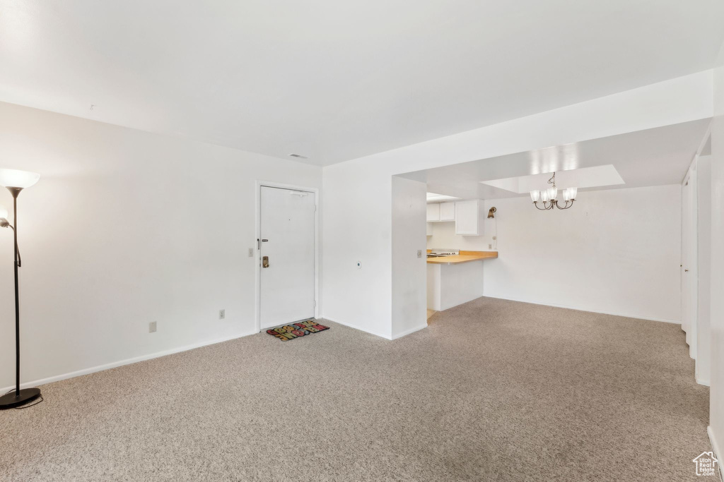 Unfurnished living room featuring light colored carpet, a chandelier, and baseboards