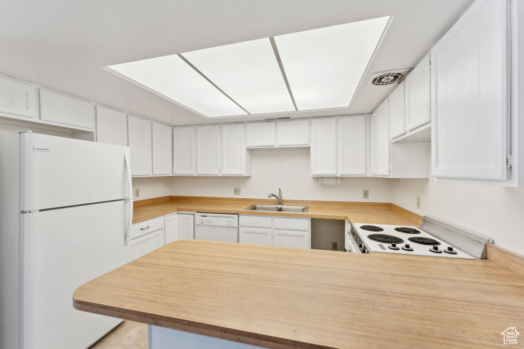 Kitchen featuring white appliances, a peninsula, a sink, light countertops, and white cabinets