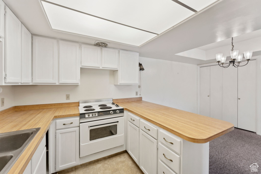 Kitchen featuring electric stove, a peninsula, white cabinets, and a sink