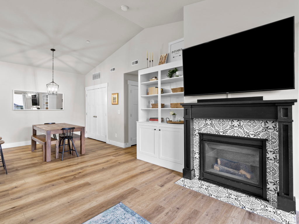 Living area featuring a tile fireplace, baseboards, light wood-type flooring, high vaulted ceiling, and a chandelier