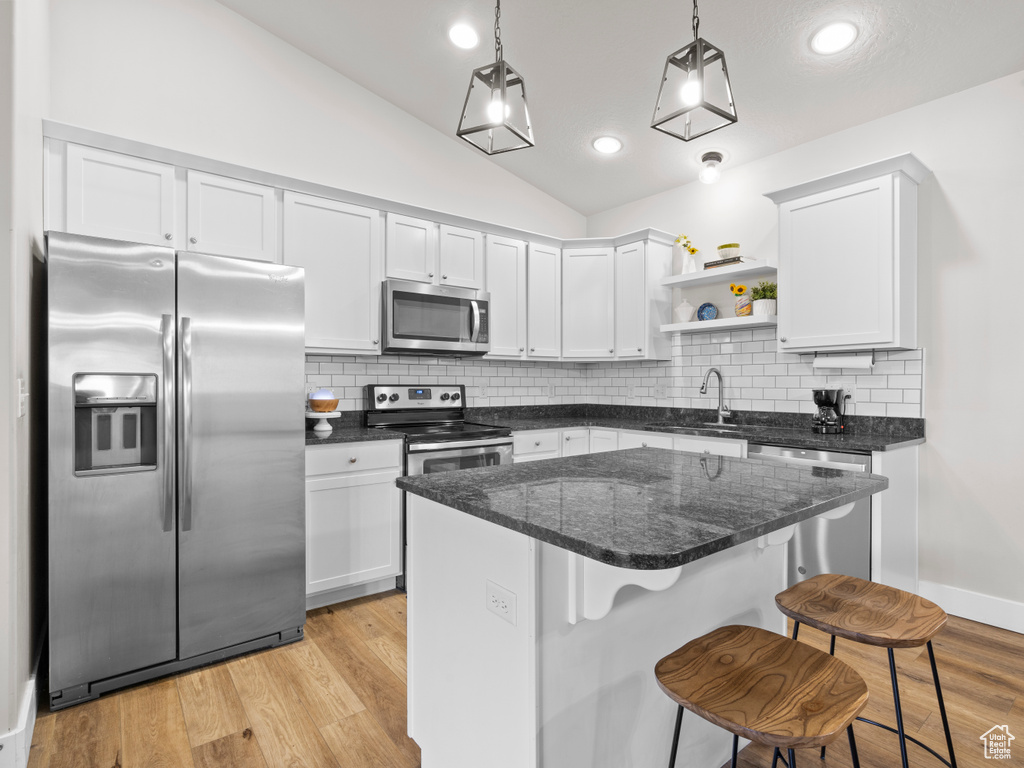 Kitchen with stainless steel appliances, open shelves, a sink, vaulted ceiling, and a kitchen breakfast bar