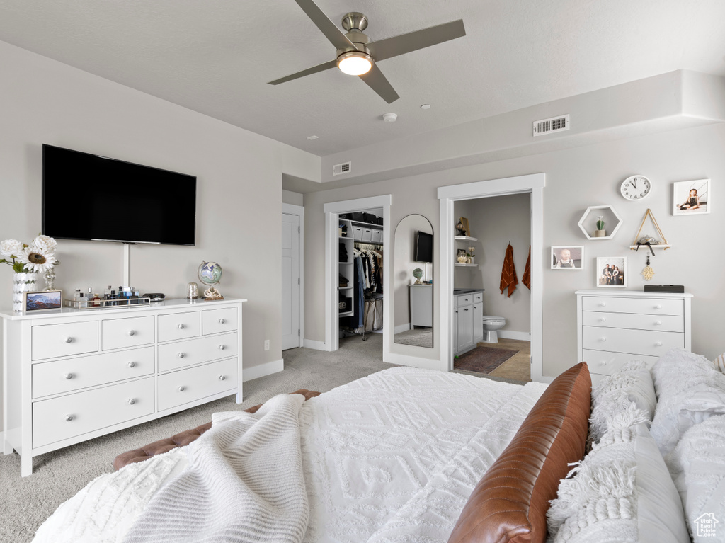 Bedroom featuring light colored carpet, baseboards, ensuite bath, a spacious closet, and a ceiling fan