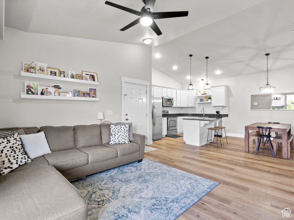 Living area with ceiling fan, light wood-style flooring, vaulted ceiling, recessed lighting, and a chandelier
