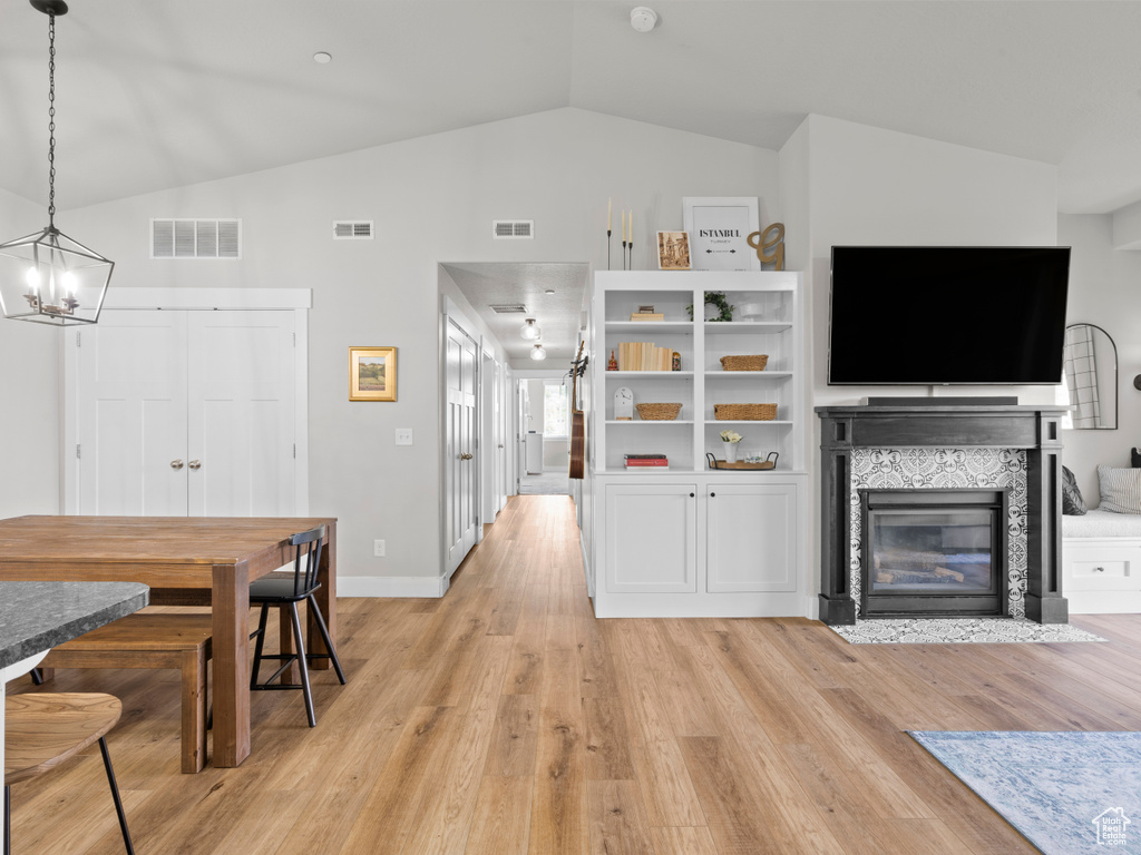 Living area with lofted ceiling, a chandelier, light wood-style flooring, a fireplace with flush hearth, and baseboards
