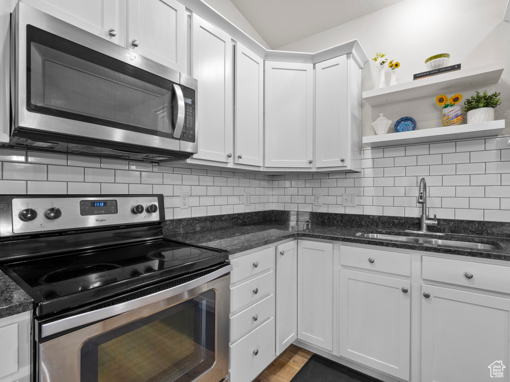 Kitchen featuring stainless steel appliances, a sink, open shelves, white cabinetry, and decorative backsplash