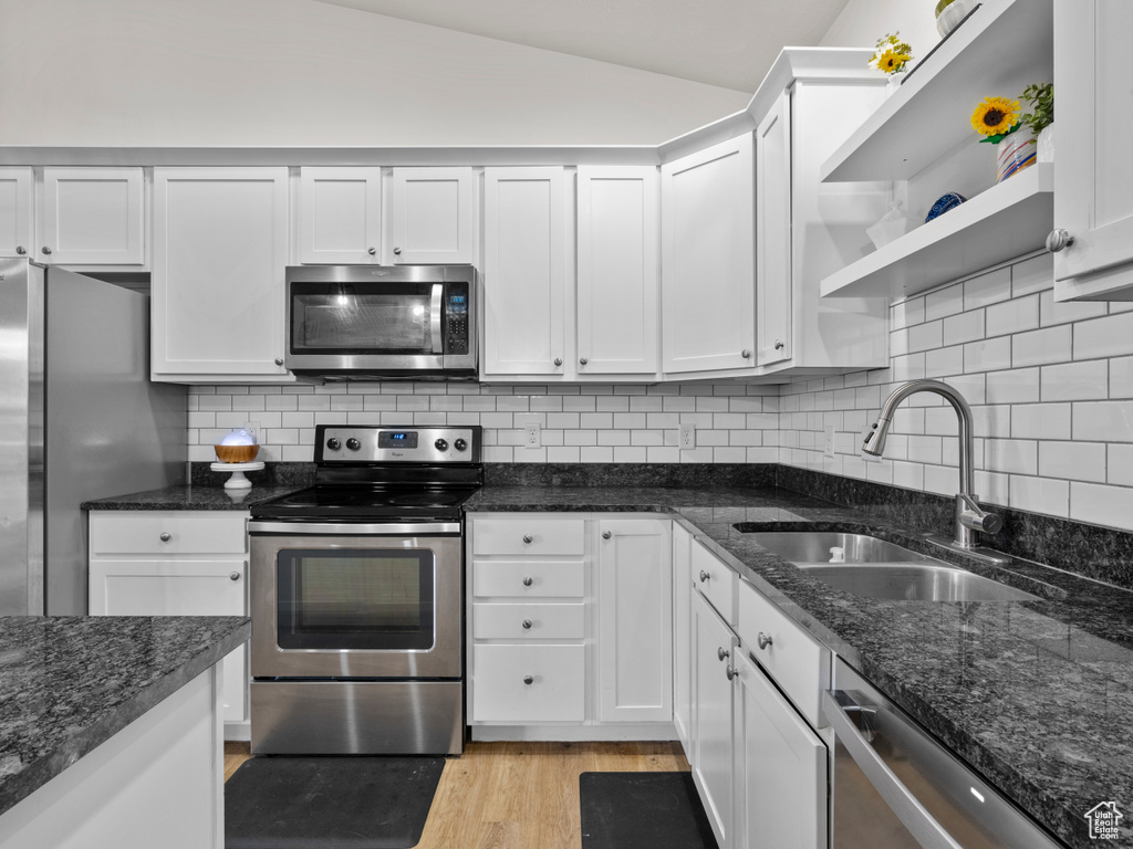 Kitchen featuring appliances with stainless steel finishes, white cabinets, a sink, open shelves, and lofted ceiling
