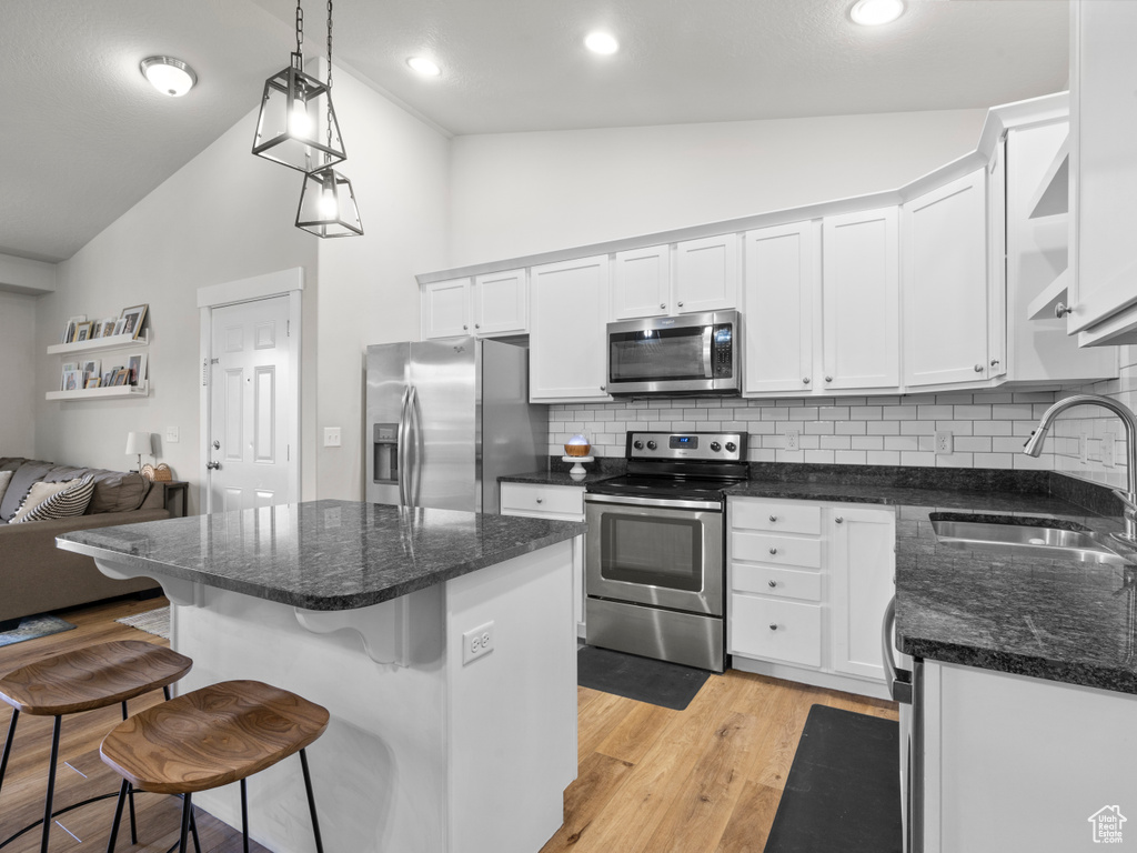 Kitchen featuring stainless steel appliances, a sink, vaulted ceiling, light wood-style flooring, and white cabinetry