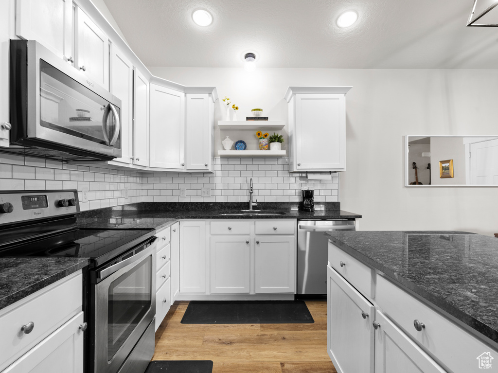 Kitchen featuring stainless steel appliances, a sink, white cabinetry, open shelves, and light wood-style floors