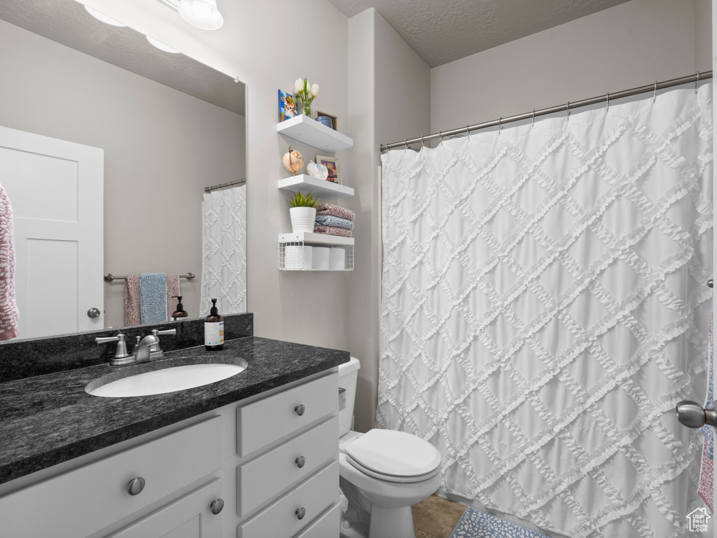 Bathroom featuring toilet, vanity, a textured ceiling, and a shower with shower curtain