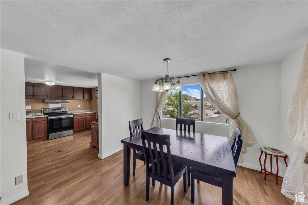 Dining room featuring a chandelier, light wood finished floors, baseboards, and a textured ceiling