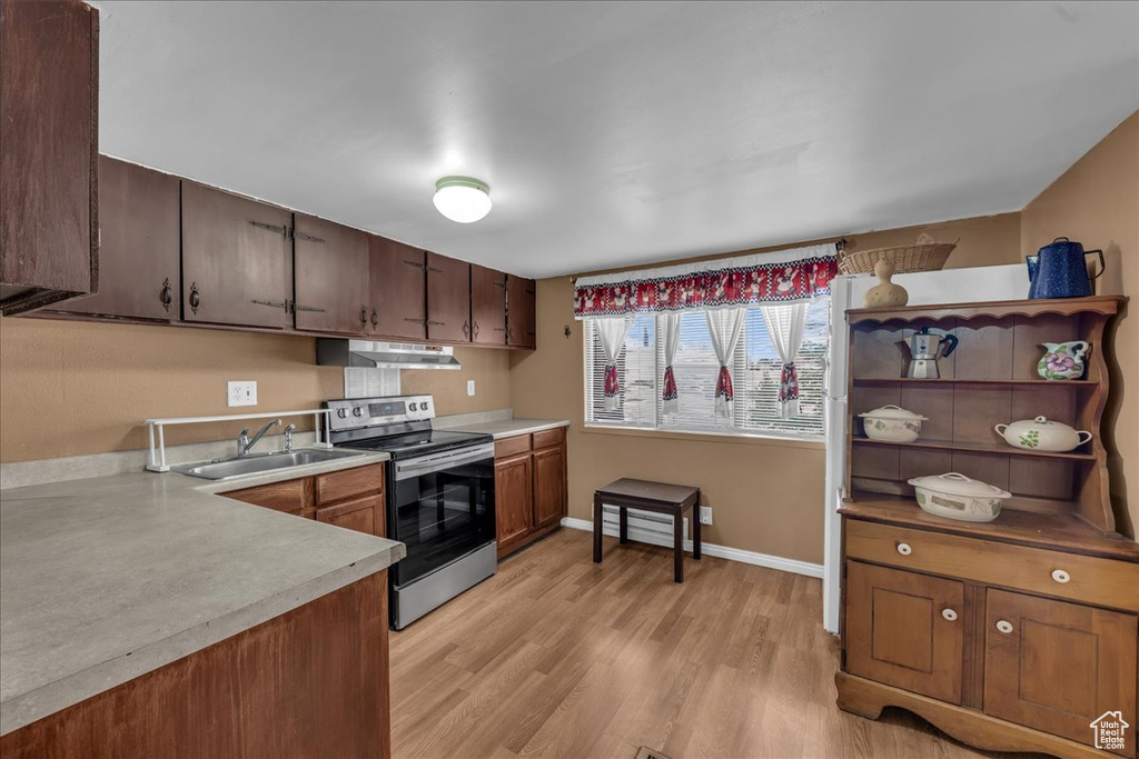 Kitchen with stainless steel electric stove, a sink, under cabinet range hood, and light countertops